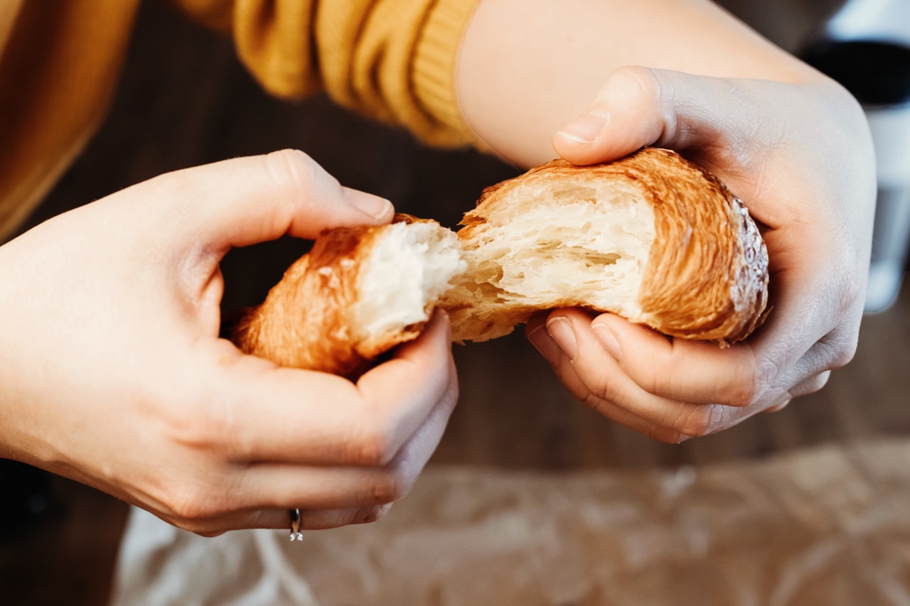 Lunch bestellen bij Brood & Banket Alsady. Vrouw breekt croissant met handen.